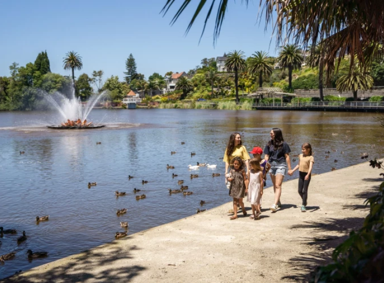 A family of 5 strolls along the walkway past the water-fountain at Rotokawau Virginia Lake