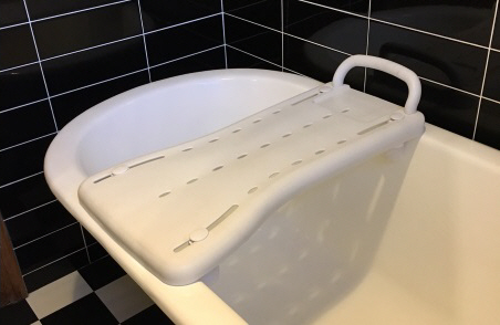 A white sturdy plastic strip about 20 cm wide fitted across the top of a bath. There is a grip handle at one end.