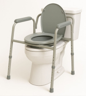 A grey metal frame that extends over a toilet with four legs set on the ground, The frame includes a raised toilet set that sits over the existing toilet. It also has arms. 